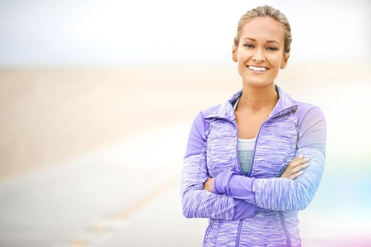 Positivity is an important aspect of health. Portrait of a young woman in sportswear standing at the beach.