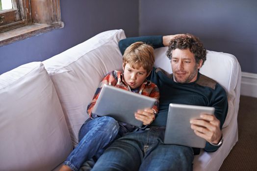 Leisure in the lounge. a father son lying on the couch together while using digital tablets.