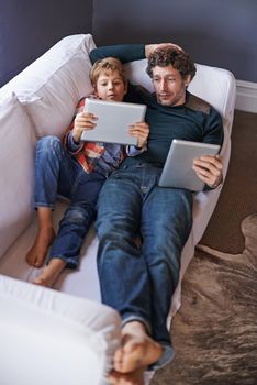 Laid-back browsing together. a father son lying on the couch together while using digital tablets.