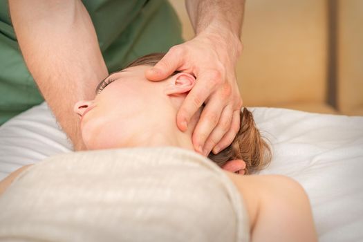 Osteopath doing massage on the female head in rehabilitation clinic center.