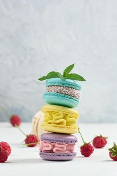 Stack of multicolored macaroons and red raspberries on a white background
