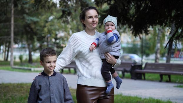 Mom with children with one-year-old and seven-year-old brothers walk down the street on an evening walk