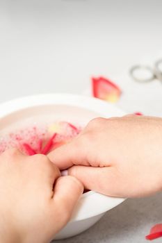 Hands in white bowl bathe nails with water and rose petals to soften the cuticle and dry skin.