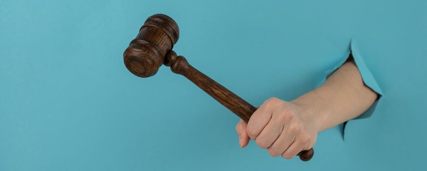 A woman's hand with a wooden judge's gavel sticks out of a hole in a blue background.