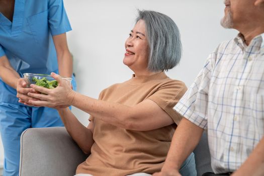 A female nurse serves a bowl of salad to a contented senior couple.