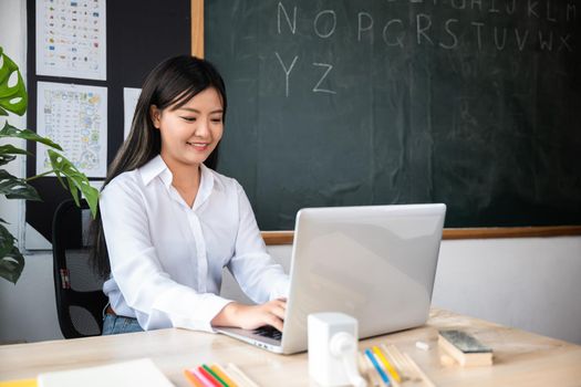 Portrait of young woman teacher with laptop at desk in classroom