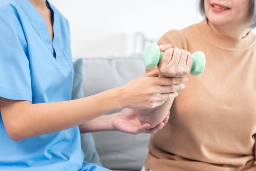 Caregiver helping contented senior woman exercise with dumbbell at home.
