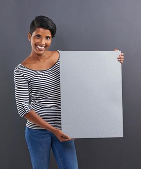 This is YOUR space. Studio shot of a beautiful young woman holding a blank placard against a grey background.