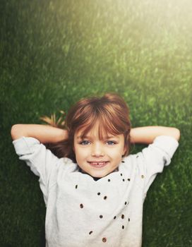 Born to be happy. a cute little girl smiling while lying down on grass.