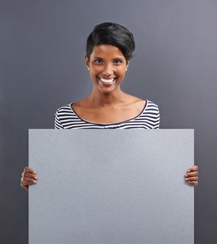 Have I got news for you. Studio shot of a beautiful young woman holding a blank placard against a grey background.