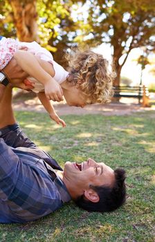Family laughter is infectious. a father lying on the grass while lifting his doughter
