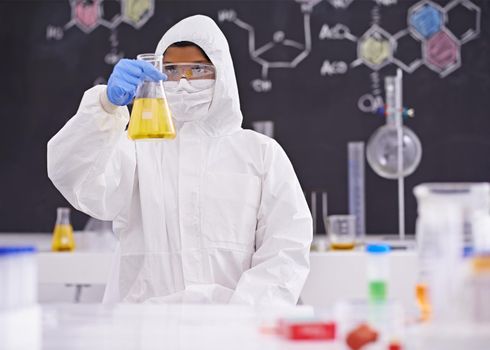 Awaiting the reaction. A young scientist in protective clothing holding up a flask in her lab.