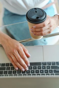 Hands typing on a computer keyboard over a white office table with a cup of coffee and supplies, top view.
