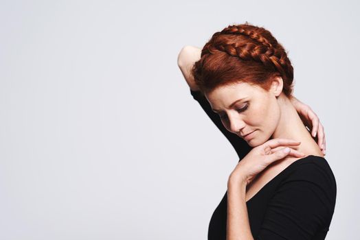 Letting her neck breathe. Studio shot of a beautiful redhead woman with a braided up-do posing against a gray background.