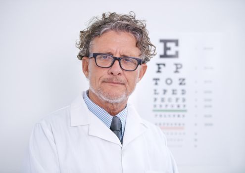Trust him to take care of your eyes. Portrait of a mature optometrist standing in front of an eye chart.
