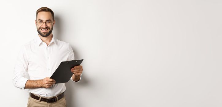 Handsome manager in glasses working, using clipboard, standing over white background