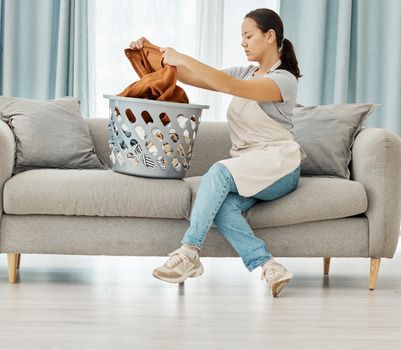 Laundry, basket and cleaning with woman folding clothes on sofa of living room at home. Housekeeping, domestic and lifestyle with young maid or housewife with fresh linen, garments or washing