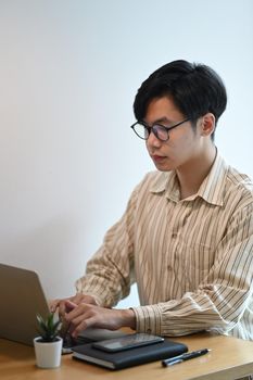 Young man in eyeglasses working with laptop in office.