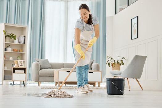 Woman cleaning the floor with a mop in the living room in home with a smile. Happy asian cleaner doing housework or job in a clean lounge, hotel room or house while smiling and alone spring cleaning