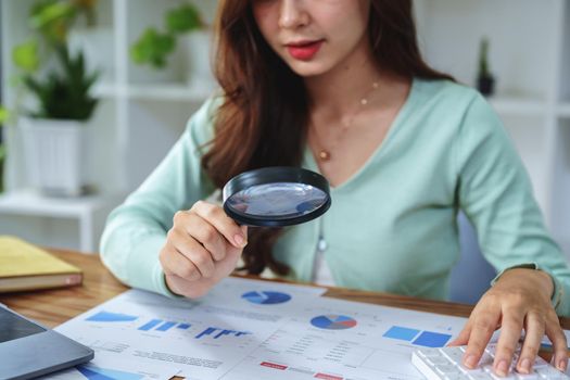 accountant holding a magnifying glass and using a calculator to check financial statements