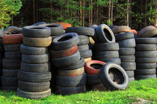 A pile of old car tires lies on the grass against the background of the forest. Ecology concept
