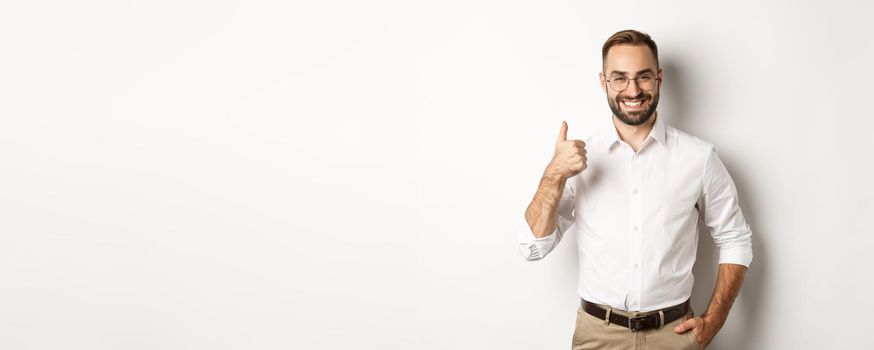 Satisfied successful boss showing thumb up, approve and praise good work, standing over white background