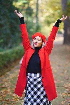 Content woman with raised arms in autumn park