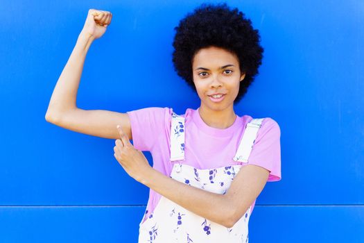 Black woman showing muscles near blue wall