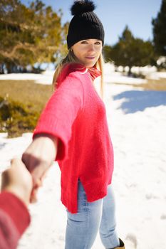 Blonde woman in winter clothes walking holding her partner's hand in the snowy mountains.