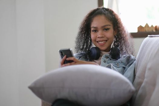 Young relaxed woman listening to the music resting on the sofa at home. Caucasian girl using smart phone and headphones for music application online.