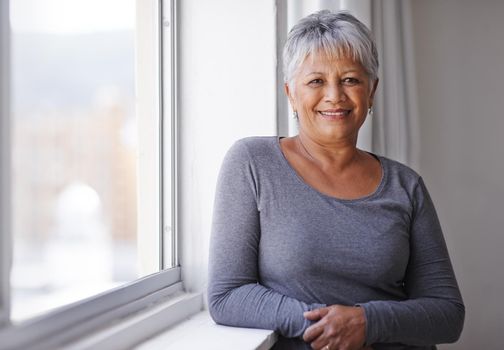 Mature and confident. Portrait of a mature woman standing by a window on a sunny day.