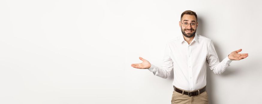 Confused smiling businessman dont know, shrugging and saying sorry, standing over white background