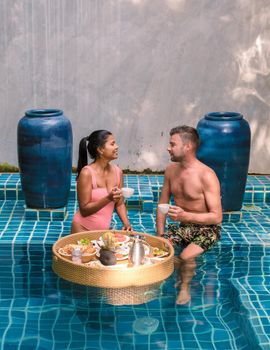 Couple having breakfast in swimming pool , Asian women and Caucasian men having floating breakfast