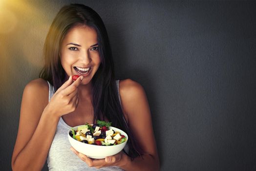 All the goodness my body needs. Portrait of a healthy young woman eating a salad against a gray background.