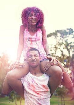 Why fit in when you were born to stand out. a young man carrying a woman on his shoulders at a color festival.
