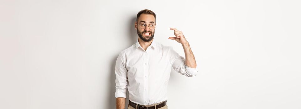 Displeased bearded man showing small gesture, looking disappointed, standing against white background
