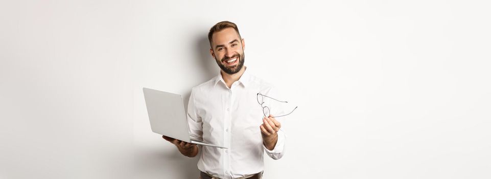 Satisfied businessman praising good job while checking laptop, standing over white background