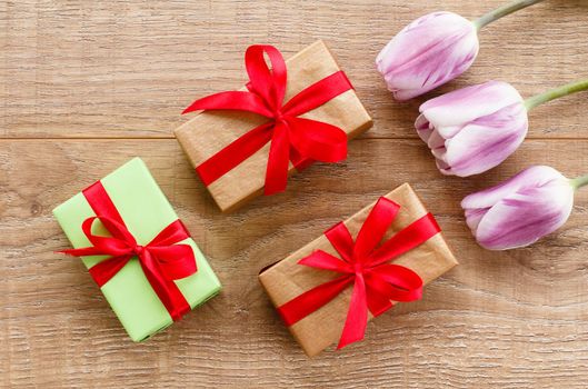 Gift boxes with red ribbons and tulips on wooden boards.