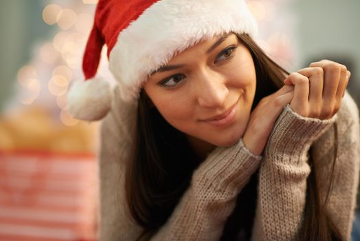 Thinking about Christmases past. an attractive young woman wearing a santa hat looking thoughtful.