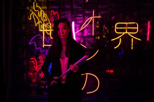 Portrait of an asian man holding a bat in a neon studio.