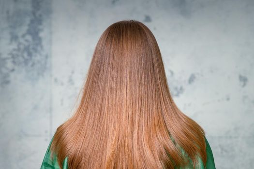 Rear View of a woman with long brown hair against a gray background.