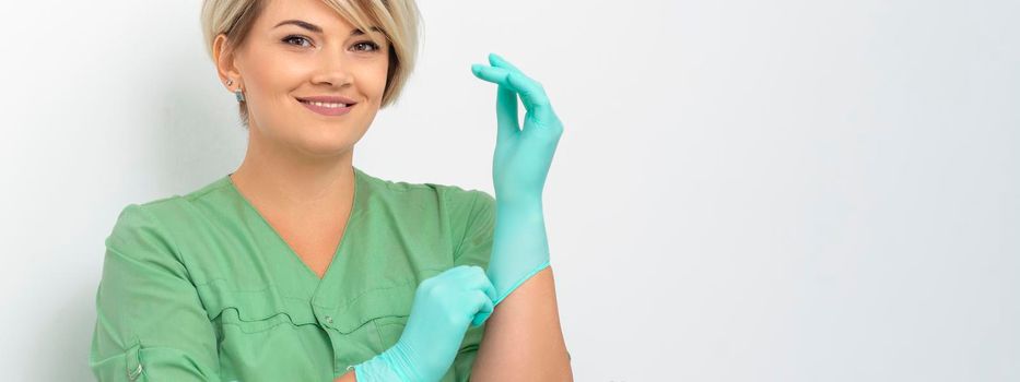 Doctor beautician puts on sterile blue gloves smiling prepares to receive clients on white.