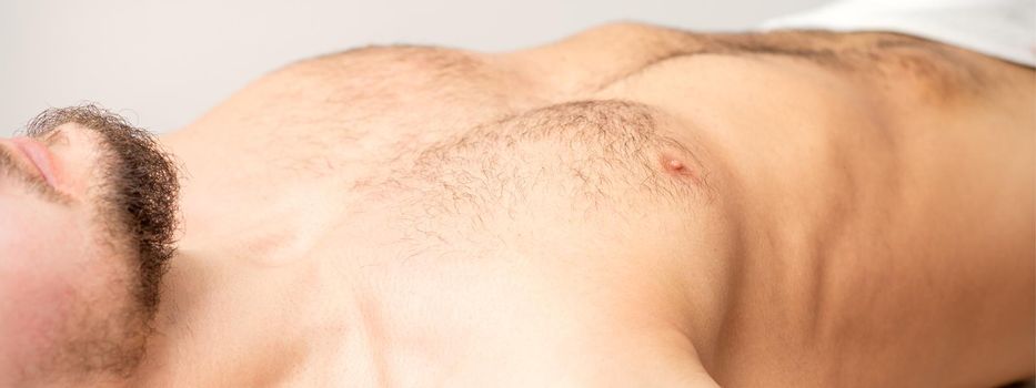 Hairy body, stomach, and chest of a man lying before epilation.