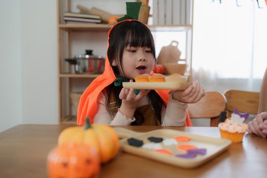 Young girl and mother at Halloween making treats and cupcake on table. Happy Halloween day