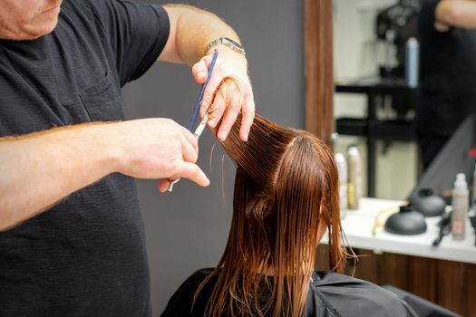 Woman having a new haircut. Male hairstylist cutting brown hair with scissors in a hair salon.