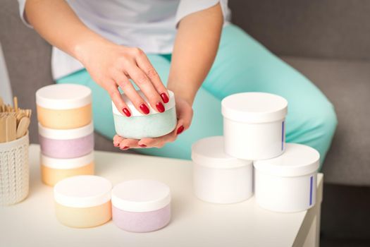 Female hands open a white body cream jar over the table with many jars of cosmetics.