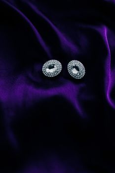 Luxury diamond earrings on dark violet silk fabric, holiday glamour jewelery present