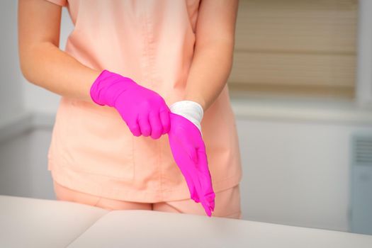 Hand of beautician puts on sterile pink gloves prepares to receive clients indoors.