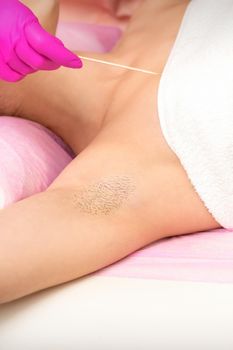 Hand in glove with spatula depilates female hairy armpit in a spa.
