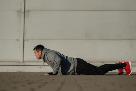 A man in a hoodie jumps while doing push-ups outdoors.